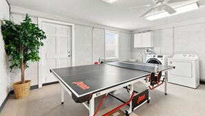 Ein Zimmer mit Tischtennisplatte, Deckenventilator, Waschmaschine und einer Pflanze.