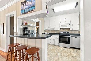 A kitchen with white cabinets, a microwave, an oven, and a coffee maker. There are three wooden stools at the counter.