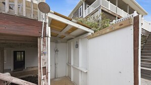 Eine Holzterrasse mit einer weißen Wand und einer Tür zu einem überdachten Bereich.