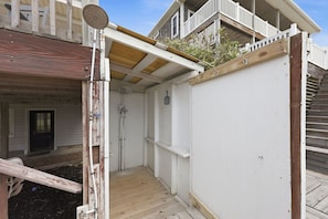A wooden deck with a white wall and a door leading to a covered area.