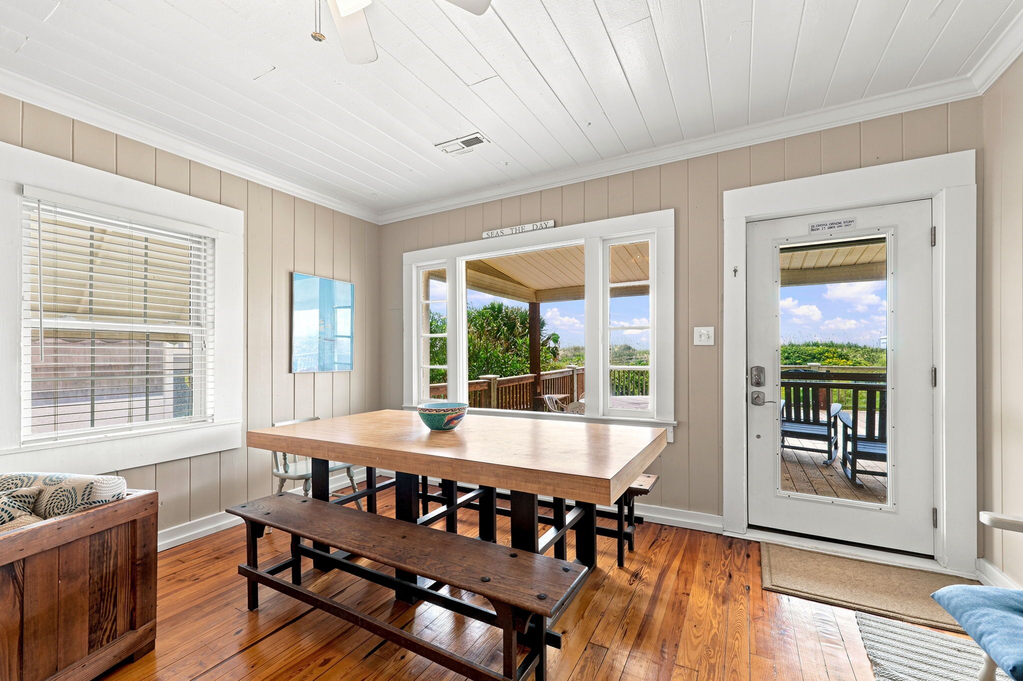 A dining area with a wooden table and bench, a window with blinds, and a door leading outside.