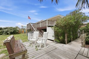 A wooden deck with white chairs and a bench, a wooden fence, and a building with a flag.