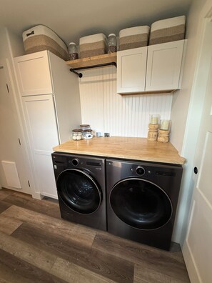 A laundry area with two front-loading washing machines, a white refrigerator, and storage shelves above. - Tranquil 3-bedroom house with AC in charming Buena Vista (Buena Vista)