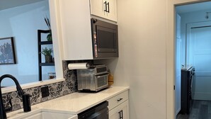 Una cocina moderna con armarios blancos, microondas integrado, lavavajillas y piso de madera.