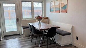 Un comedor con una mesa de madera, sillas negras, un banco y un jarrón con flores.