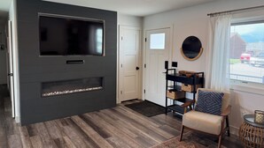Una sala de estar moderna con televisor de pantalla plana, chimenea, sofá, mesa de centro y ventana con vistas.