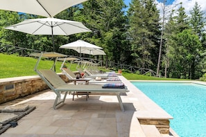A poolside area with lounge chairs and umbrellas, surrounded by trees. - Villa Palazzolo 8, Emma Villas (Anghiari)