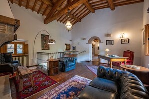 A spacious living room with a high ceiling, leather furniture, a staircase, and a dining area. - Villa Palazzolo 8, Emma Villas (Anghiari)