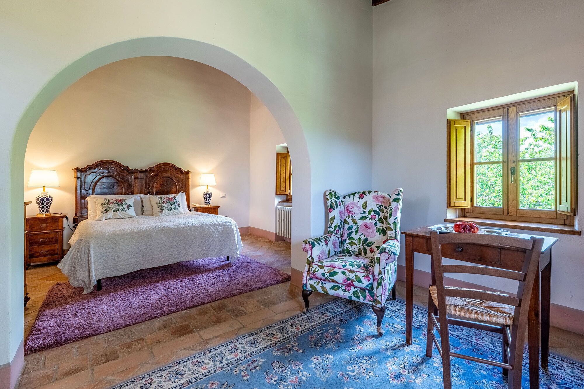 Une chambre à coucher avec un lit, une chaise, un bureau, une fenêtre et un radiateur.