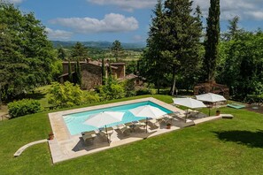 A swimming pool with lounge chairs and umbrellas, surrounded by lush greenery and a stone building. - Villa Palazzolo 8, Emma Villas (Anghiari)
