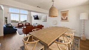 Un vaste espace de vie comprenant une grande table à manger en bois, entourée de chaises en osier, d’un canapé bleu et d’un fauteuil rouge.