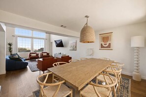 A spacious living area with a large wooden dining table surrounded by wicker chairs, a blue sofa, and a red armchair. - Desert Sunsets Wellness Villa - Pool, Sauna, Spa, Pool Table, Firepit, Yoga, Steam Room & Stunning Views (Yucca Valley)