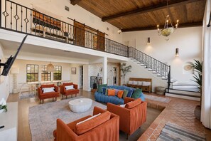 A spacious living area with a high ceiling, a staircase, and a balcony. - Desert Sunsets Wellness Villa · Pool, Sauna, Views (Yucca Valley)