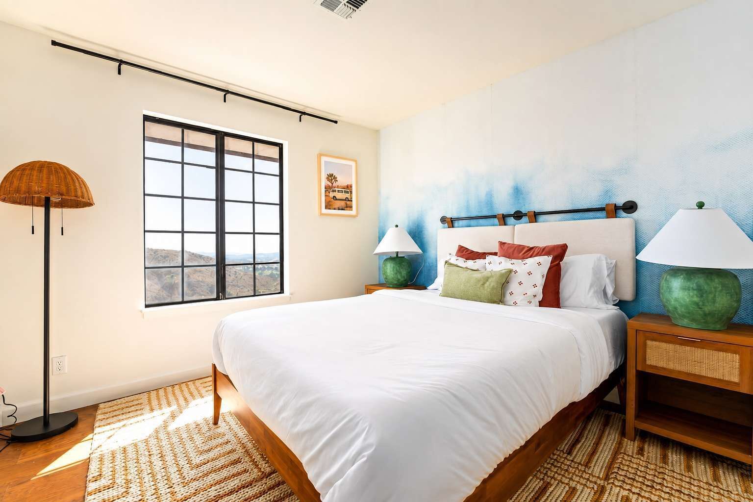 Quarto com uma cama grande, janela com vista, luminária e um quadro na parede.