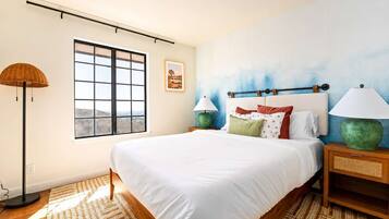 Quarto com uma cama grande, janela com vista, luminária e um quadro na parede.