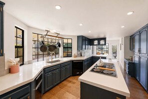 A modern kitchen with dark cabinetry, a central island, and a window overlooking a garden.