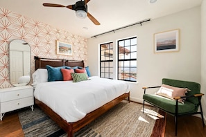 A bedroom with a bed, a chair, a dresser, a mirror, and a ceiling fan. - Desert Sunsets Wellness Villa - Pool, Sauna, Spa, Pool Table, Firepit, Yoga, Steam Room & Stunning Views (Yucca Valley)