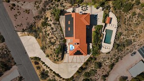An aerial view of a property with a swimming pool, a covered patio, and a large open space with a red-roofed building. - Desert Sunsets Wellness Villa · Pool, Sauna, Views (Yucca Valley)