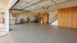 A garage with a concrete floor, a wooden staircase, and a workbench with tools. - Desert Sunsets Wellness Villa - Pool, Sauna, Spa, Pool Table, Firepit, Yoga, Steam Room & Stunning Views (Yucca Valley)