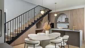 Una cuina moderna amb una illa central, una zona de menjador amb sis cadires, una escala amb baranes negres i il·luminació penjant.