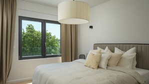 Un dormitori amb un llit gran, una finestra amb cortines i una làmpada penjant.