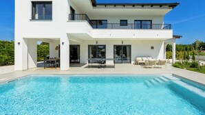 Una casa moderna de dos pisos amb piscina, zona d'estar a l'exterior i un balcó.