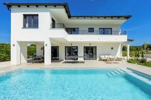 Ein modernes, zweistöckiges Haus mit Pool, Sitzgelegenheiten im Freien und einem Balkon.