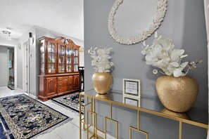 Een hal met een houten kast, een gouden console tafel met vazen en een blauw kamerkleed.