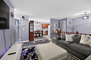 A living room with a sofa, ottoman, and a TV on a stand. - Cozy Townhome Near Downtown & Target Field (Minneapolis)