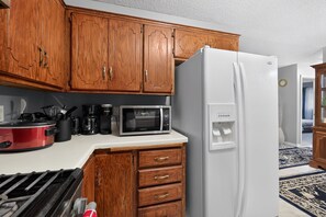 A kitchen with wooden cabinets, a white refrigerator, a microwave, and a red slow cooker. - Cozy Townhome Near Downtown & Target Field (Minneapolis)