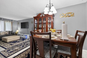 A dining area with a wooden table, chairs, a chandelier, and a decorative wall piece. - Cozy Townhome Near Downtown & Target Field (Minneapolis)