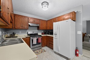 A kitchen with wooden cabinets, a stainless steel sink, a stove, a refrigerator, and a fire extinguisher. - Cozy Townhome Near Downtown & Target Field (Minneapolis)
