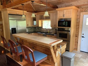 A wooden cabin interior with a kitchen featuring a refrigerator, microwave, oven, and a large island with chairs.