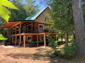 A two-story log cabin with a green roof, multiple balconies, and a porch area.