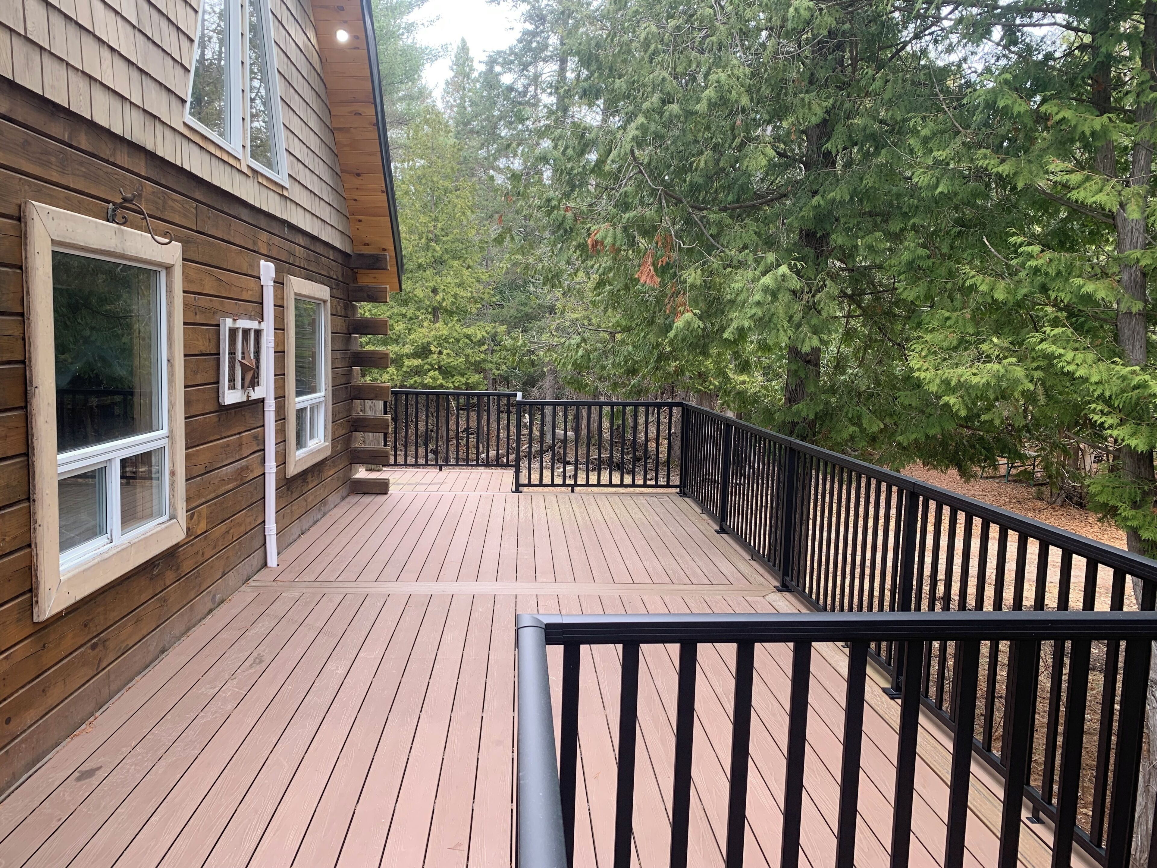 Une terrasse en bois avec des rampes noires, entourée d’arbres.