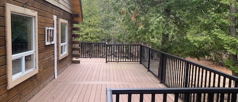 Une terrasse en bois avec des rampes noires, entourée d’arbres.