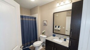 Een badkamer met toilet, wastafel, donkere kastjes, een spiegel en douchegordijn.