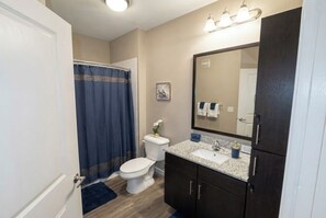 Un baño con inodoro, lavabo, armarios oscuros, un espejo y una cortina de ducha.