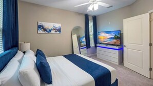 Een slaapkamer met een bed, een plafondventilator, een televisie, een dressoir en een deur.