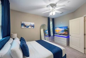 Un dormitorio con cama, ventilador de techo, televisión, cómoda y una puerta.