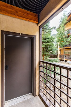 A door with a keypad lock, a balcony with a metal railing, and a view of a building with trees and a deck. - Lake Fork Ski-In Creekside w Gas Stove, Parking (Taos Ski Valley)