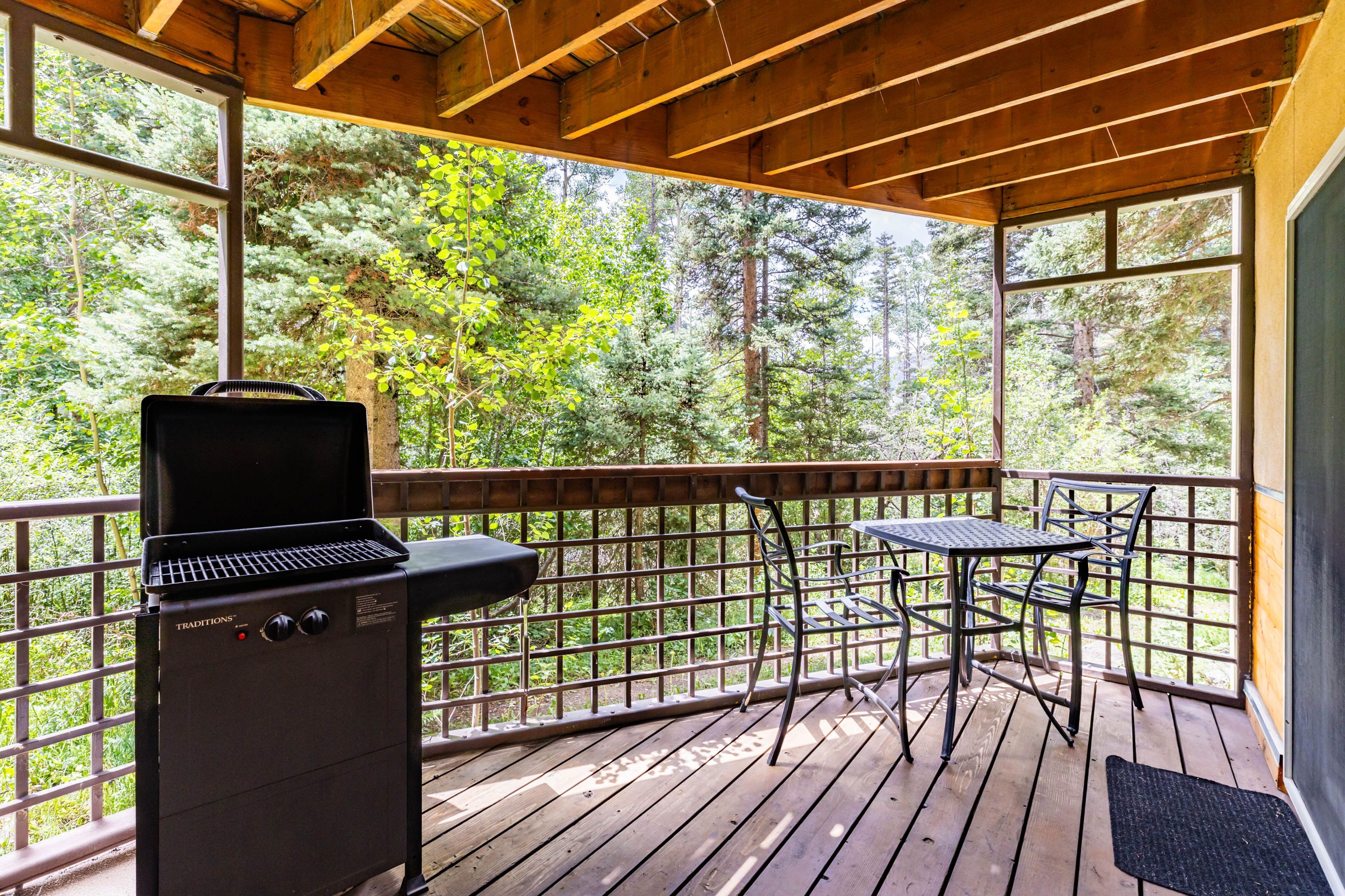 A covered outdoor deck with a grill, a table, and chairs.