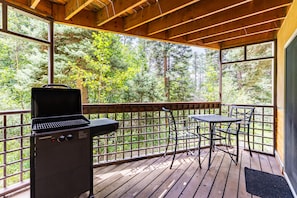 Eine überdachte Terrasse im Freien mit Grill, Tisch und Stühlen.