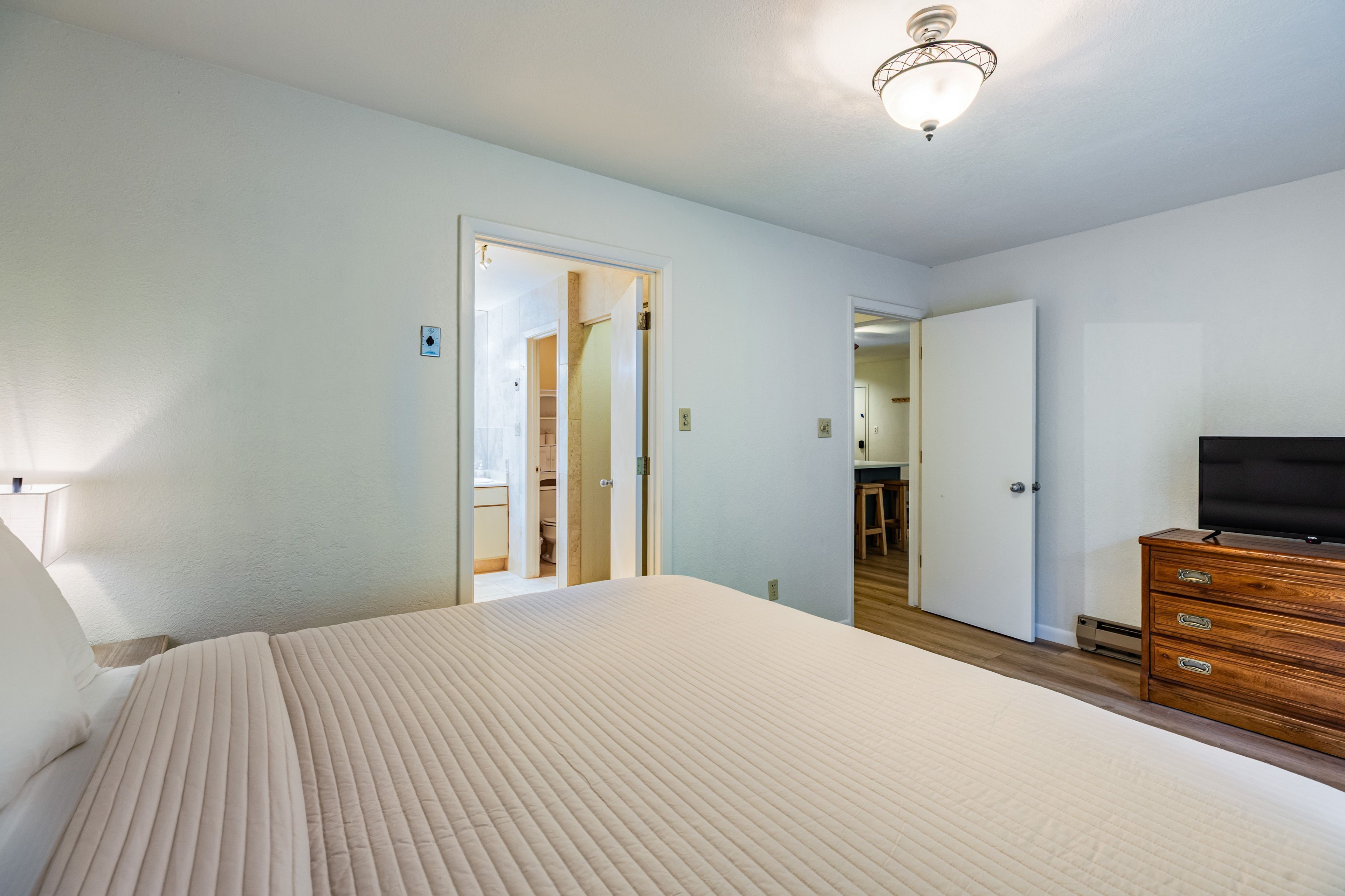 Une chambre à coucher avec un lit, une commode, une télévision, et une salle de bain visible à travers une porte ouverte.