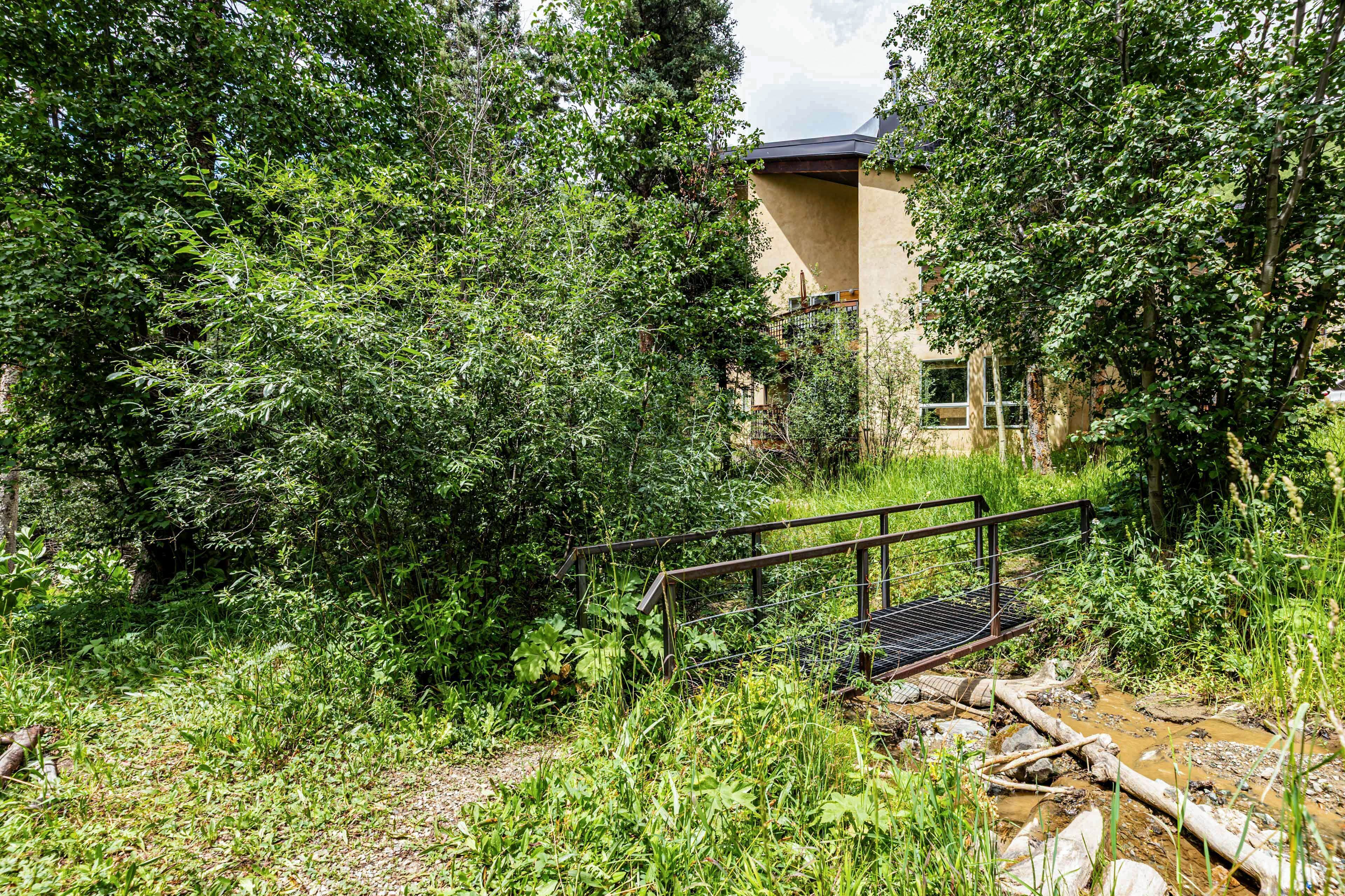 A natural landscape with dense foliage, a metal bridge, and a building with a sloped roof.