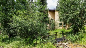 A natural landscape with dense foliage, a metal bridge, and a building with a sloped roof. - Lake Fork Ski-In Creekside w Gas Stove, Parking (Taos Ski Valley)
