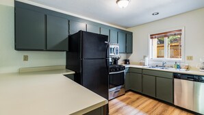 A kitchen with dark cabinets, a black refrigerator, a stove, and a dishwasher. - Lake Fork Ski-In Creekside w Gas Stove, Parking (Taos Ski Valley)