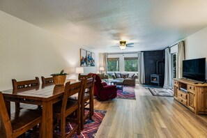A spacious living area with a wooden dining table, a sofa, a TV, and a fireplace. - Lake Fork Ski-In Creekside w Gas Stove, Parking (Taos Ski Valley)