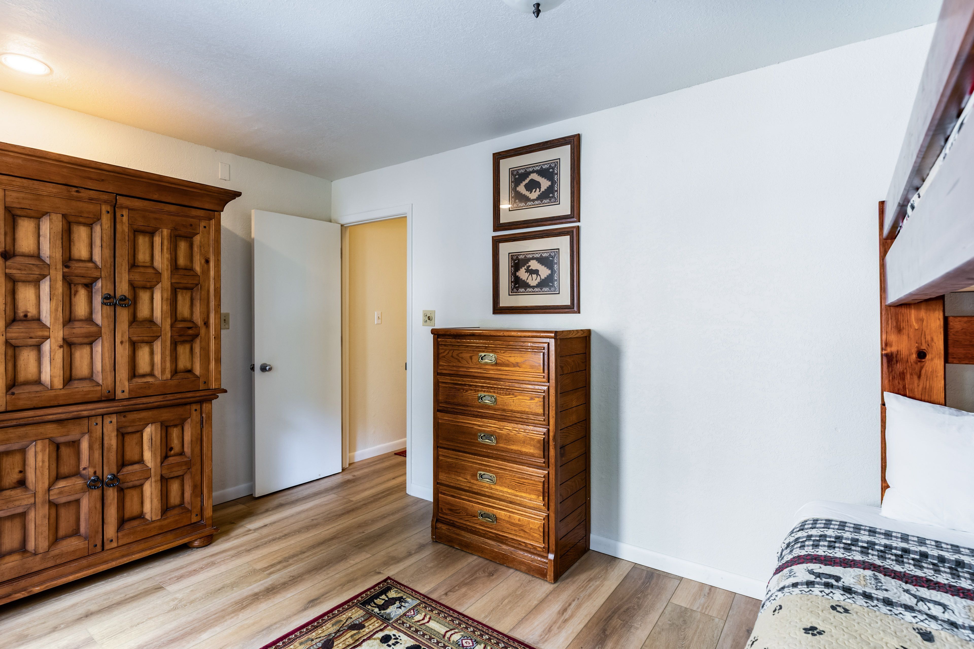 A room with a wooden wardrobe, a dresser, and a patterned rug.