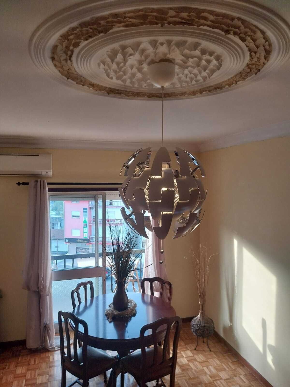 A dining area with a round table, chairs, a decorative ceiling, and a view through a window.